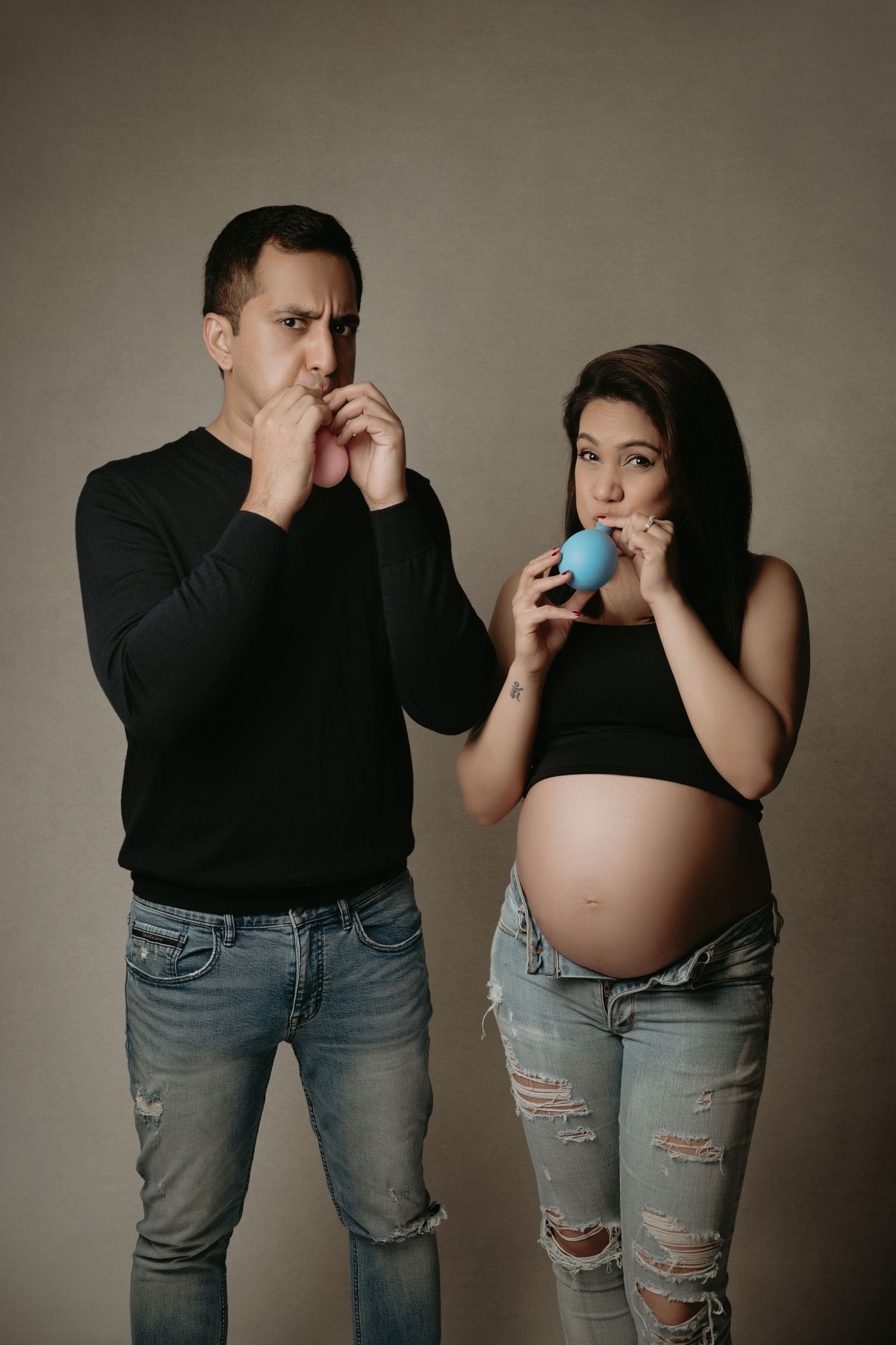 A series of maternity photos showing a couple in jeans and black tops posing together against a neutral background.