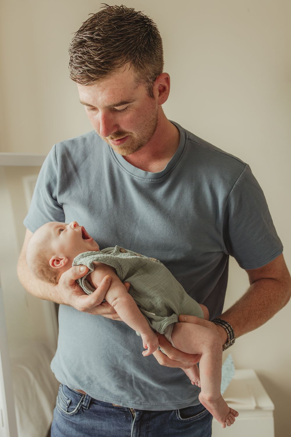 A parent in a blue t-shirt cradles and plays with a small infant.