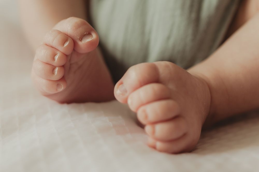 Close-up shots of tiny newborn baby feet and toes against white fabric.