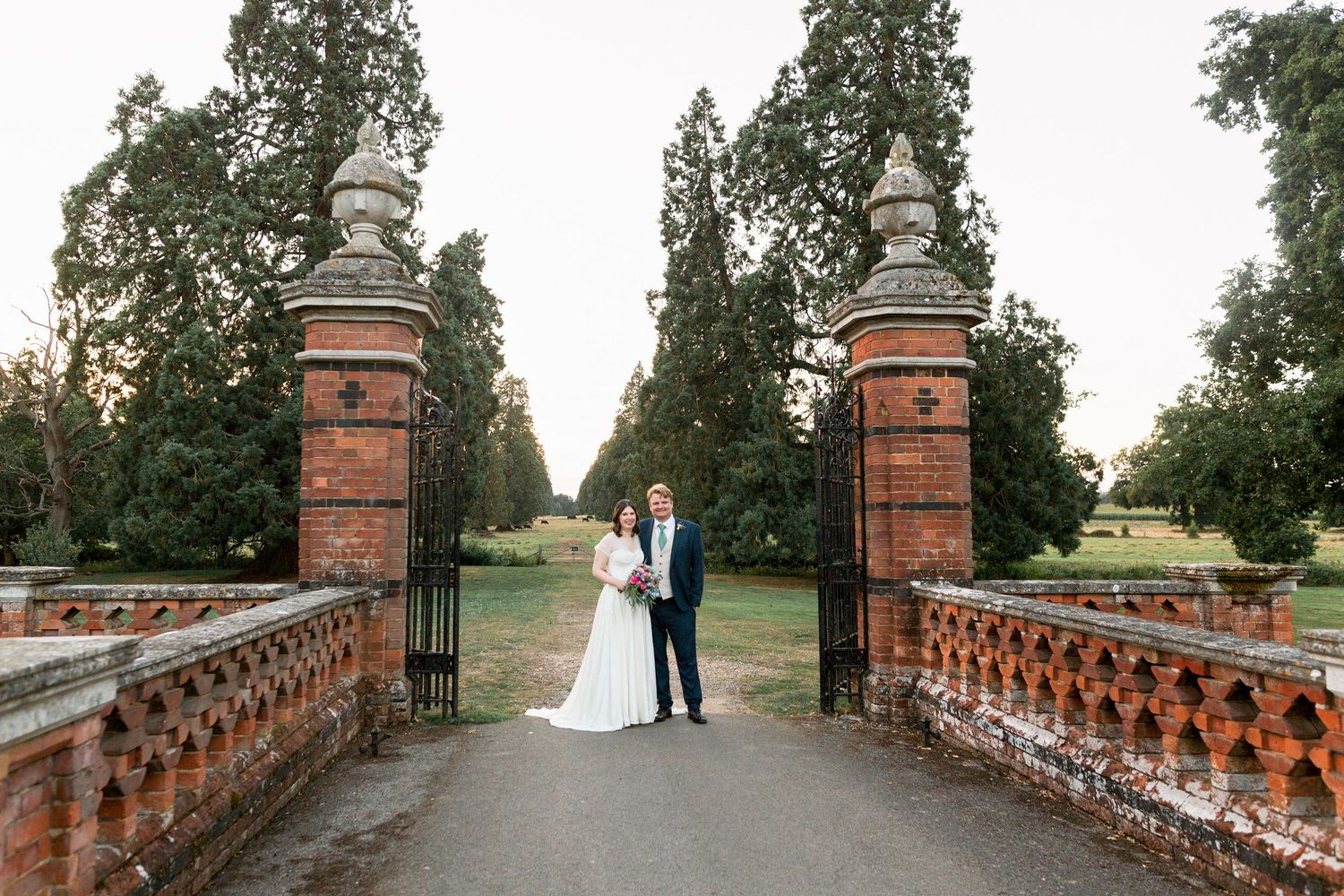 A couple poses on a rustic brick bridge during sunset at their outdoor wedding celebration.