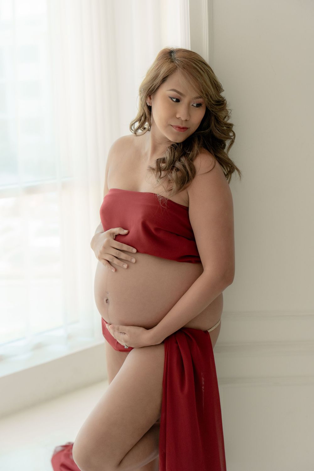 Elegant maternity boudoir session with red fabric in bright natural window light.
