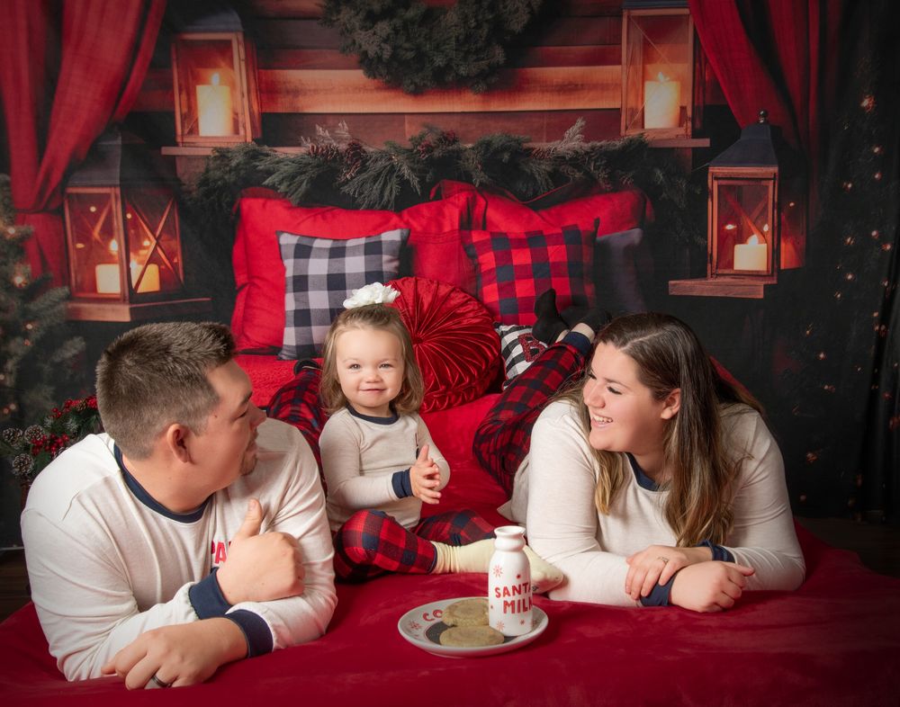 Cozy holiday scene with family lounging on red blankets surrounded by lanterns and buffalo plaid pillows in Christmas setting.