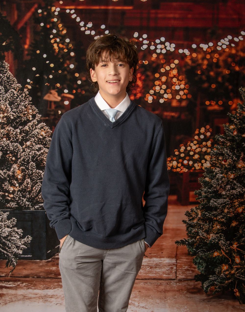 A cozy winter portrait featuring a navy sweater and grey pants against a warm glowing background with holiday decorations.