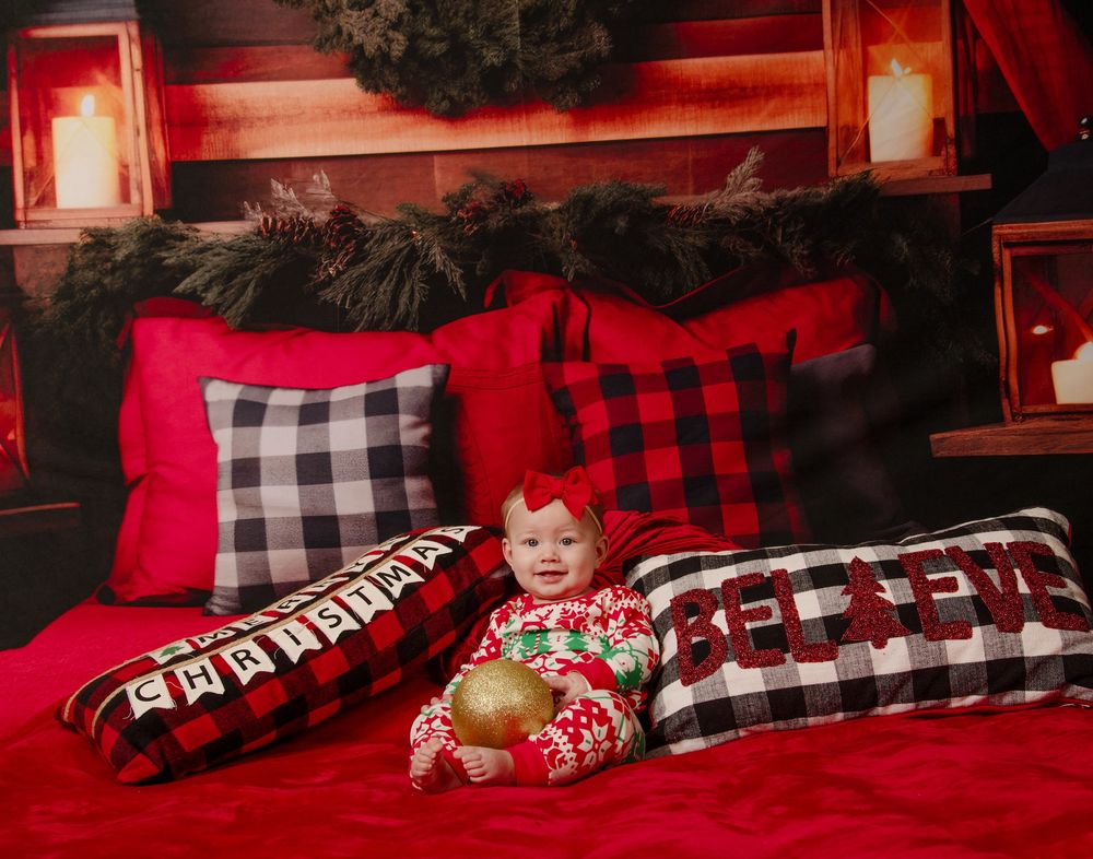 A baby lies on red and black buffalo plaid bedding with festive holiday pillows and blankets.
