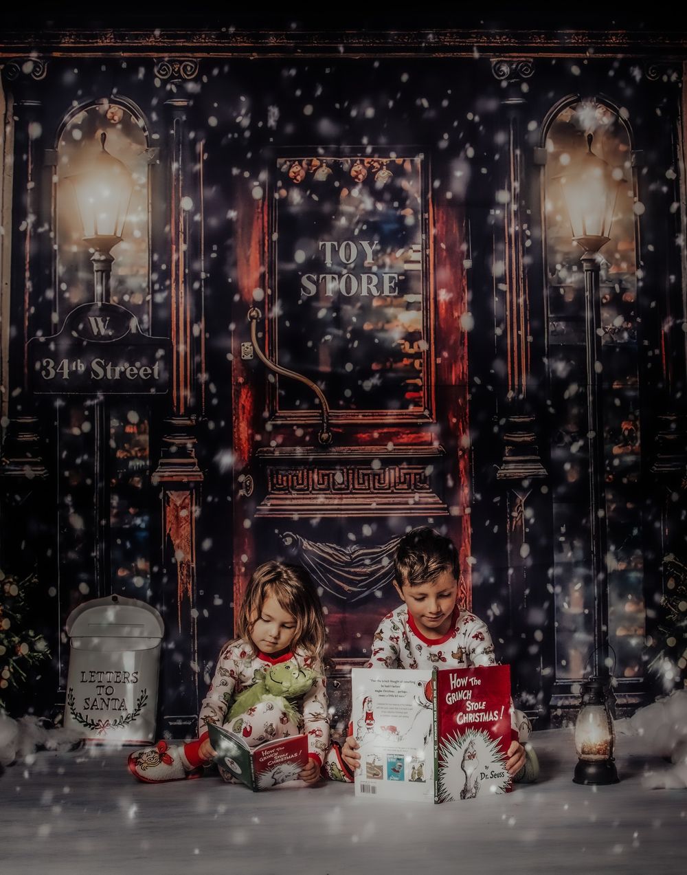 Children sit among holiday decorations and twinkling lights in front of a festive storefront display.