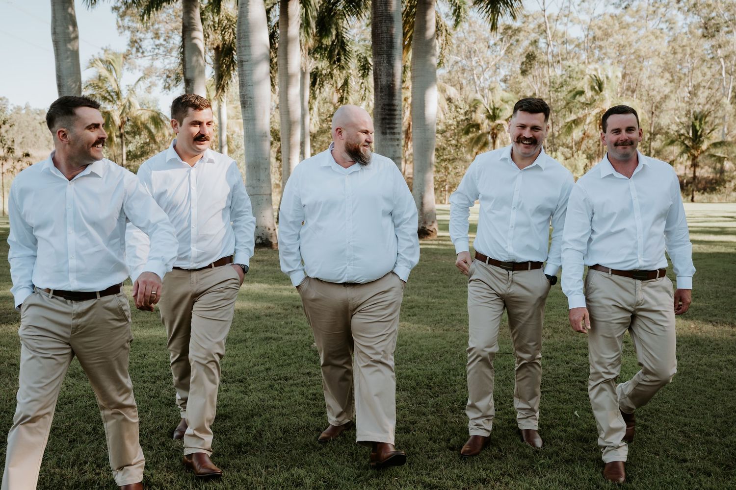 Gladstone groomsmen walking in coordinated khaki pants and light blue shirts outdoors.