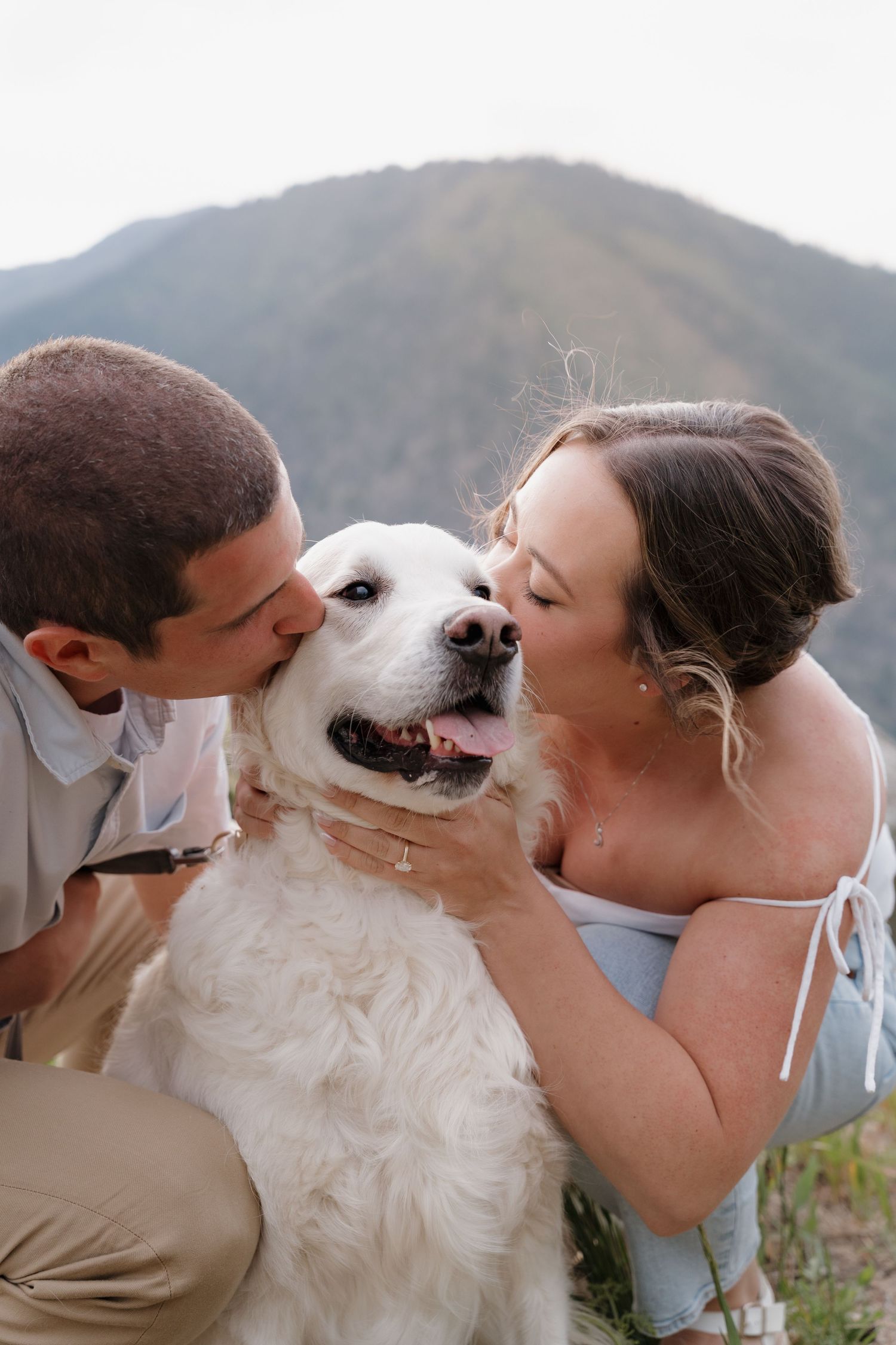 A couple shares affectionate moments with their white dog against a mountain backdrop in a series of photos.
