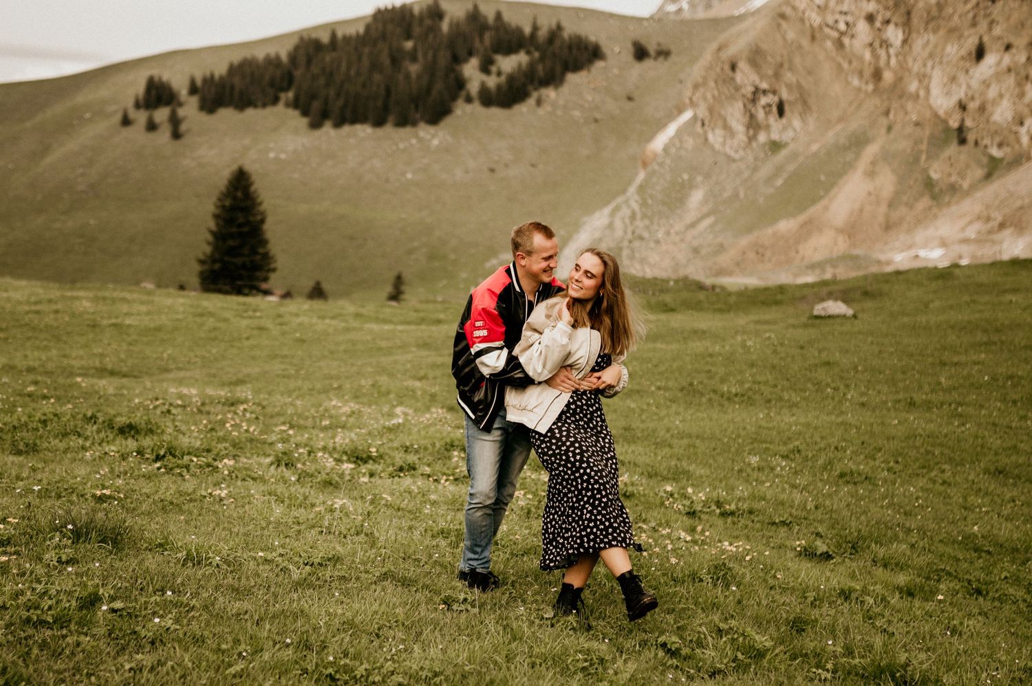 Couple dancing together in a meadow with mountains in the background.