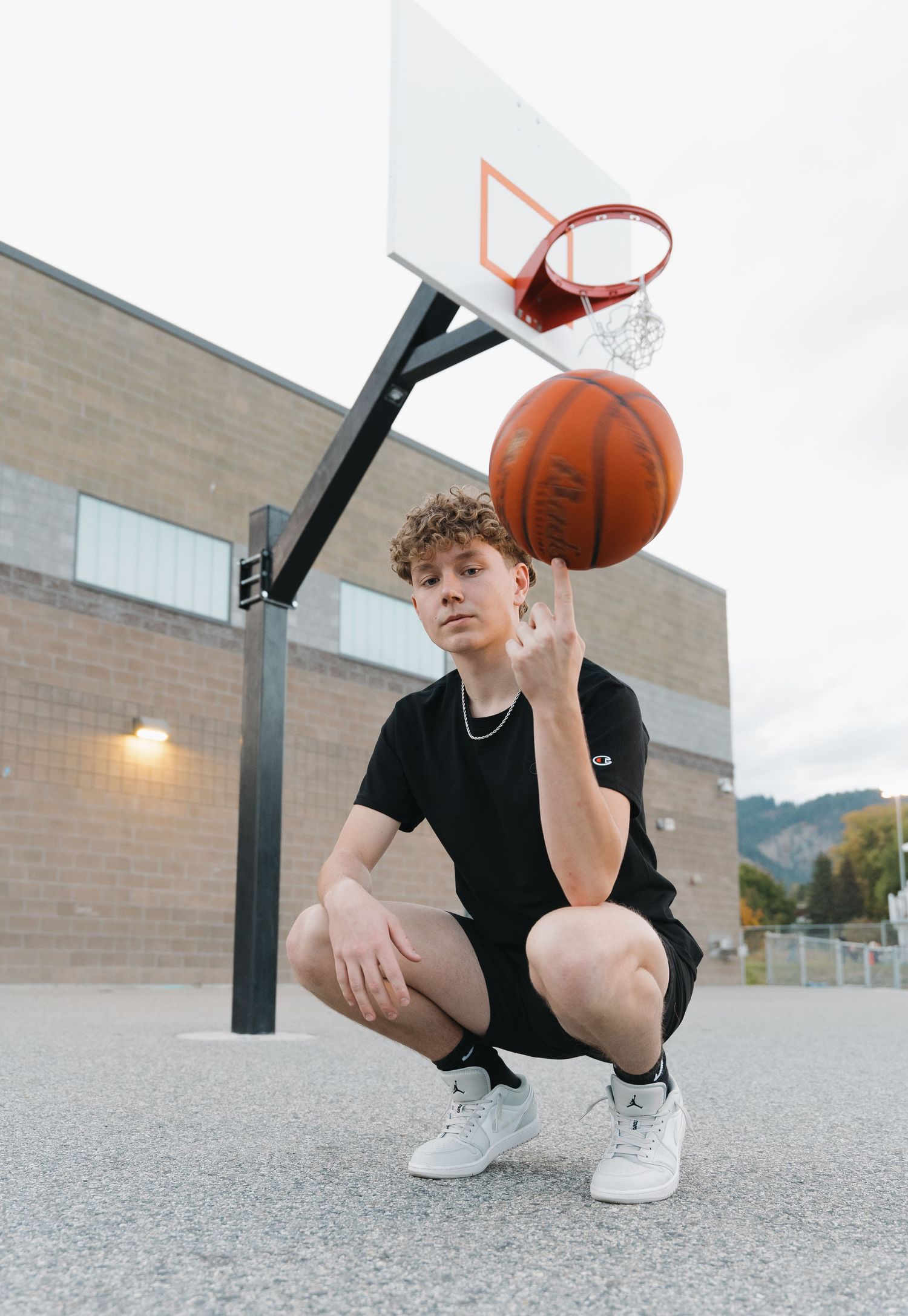 Person in black outfit crouching next to basketball hoop on outdoor court.