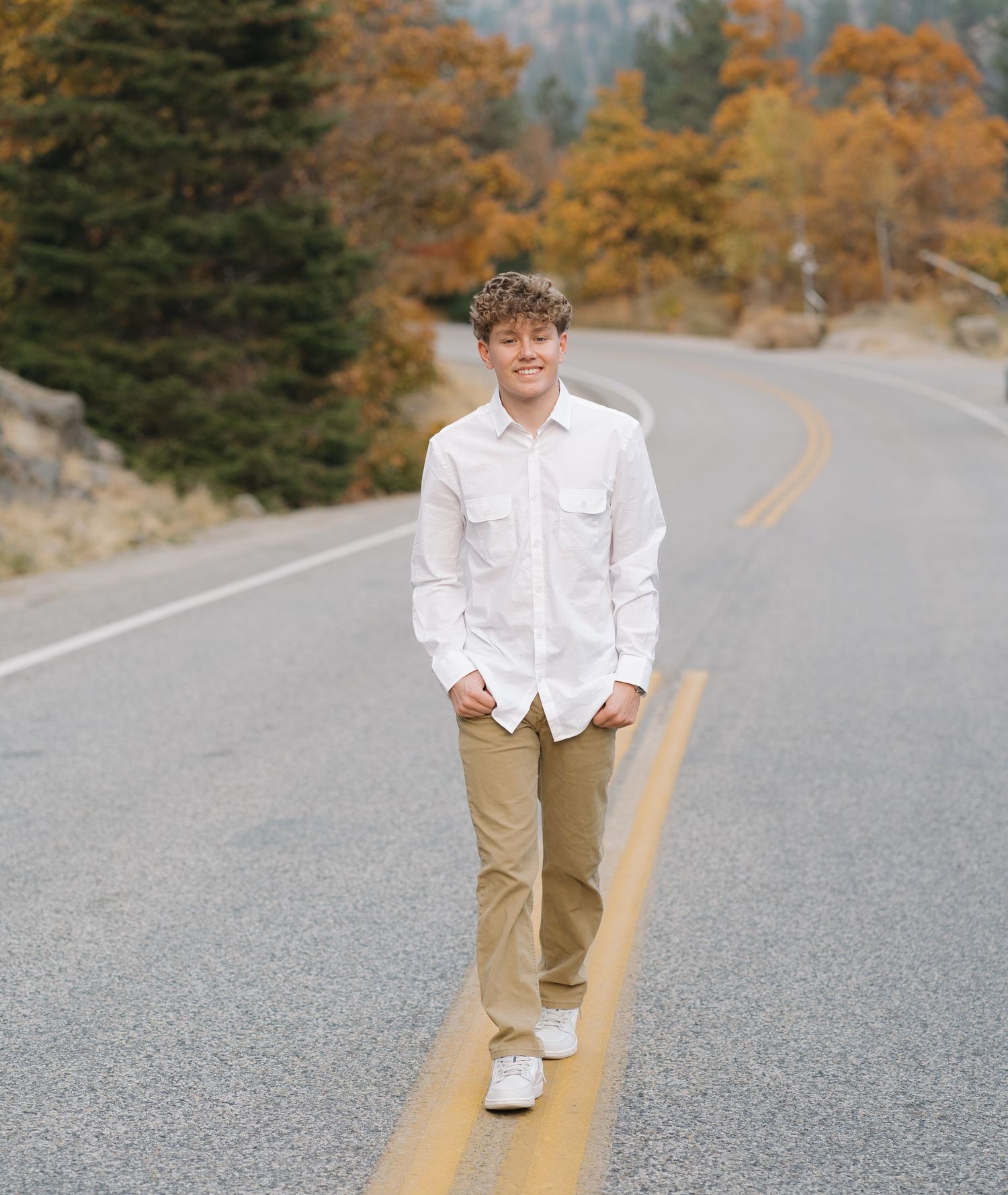 A person in white shirt and khakis stands on a mountain road surrounded by fall foliage.
