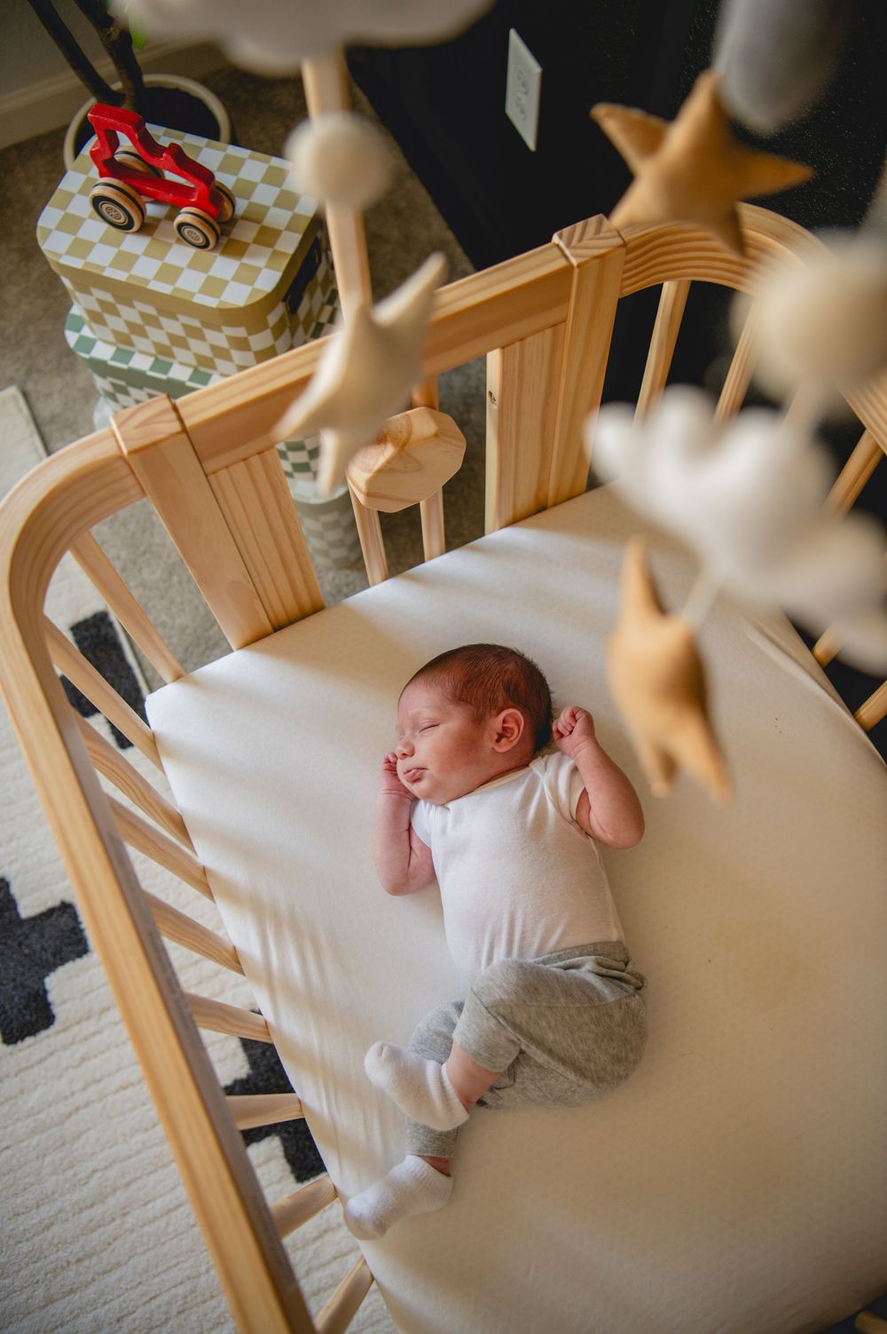 Baby sleeping peacefully in a wooden crib with white bedding and star-shaped decorations hanging above.