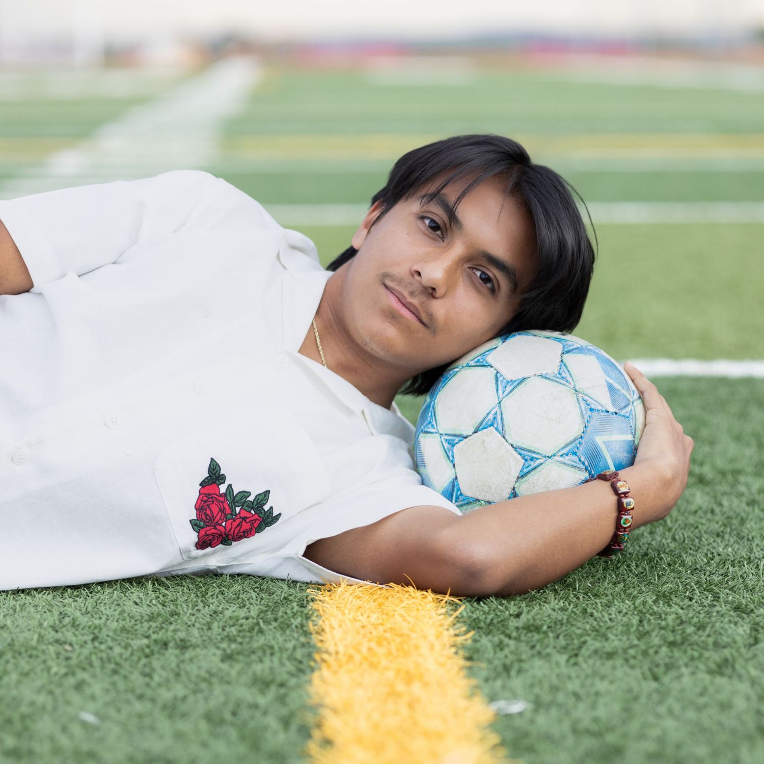 Young soccer player lying on turf field with blue and white soccer ball next to field markings.