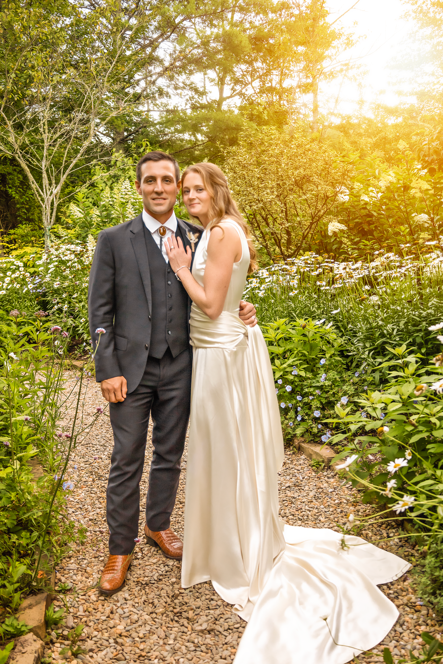 A couple poses for romantic sunset wedding photos along a garden path surrounded by lush greenery.
