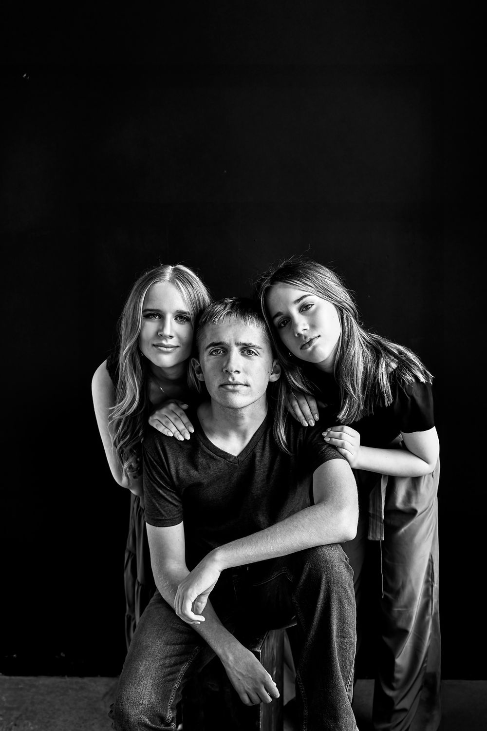 Artistic black and white portrait of three people in casual wear against dark background.