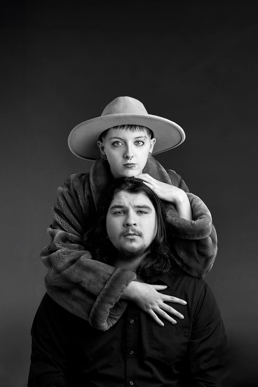 Dramatic black and white portraits showing two people in dark coats and wide-brimmed hats.