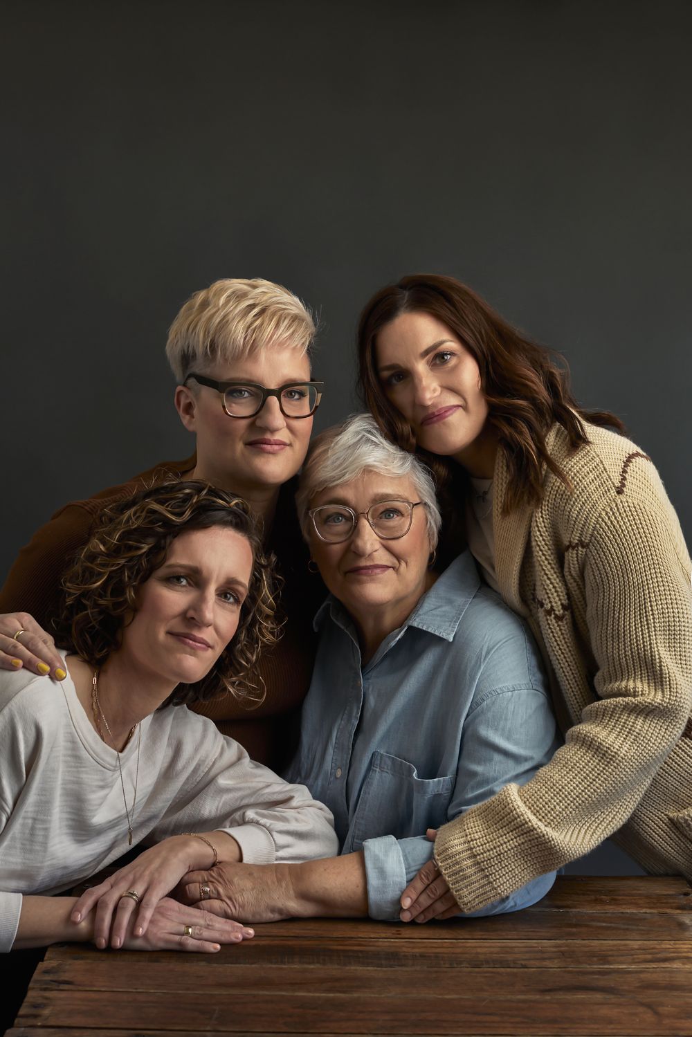 Warm portrait series of three people leaning on wooden table in casual poses.