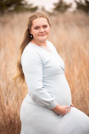 Person in white sweater dress poses in autumn field with golden grass at sunset.