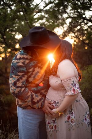 A couple embraces in a romantic sunset photoshoot with golden sunlight streaming through trees in the background.