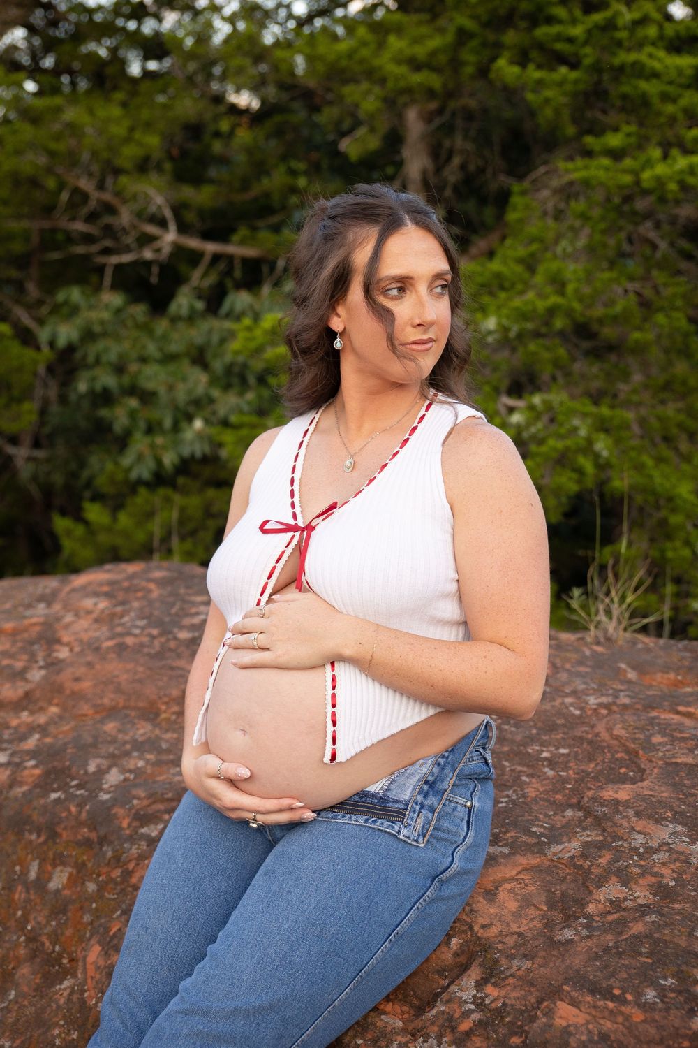 Maternity photo session outdoors on red rocks with a white top and blue jeans in natural lighting.