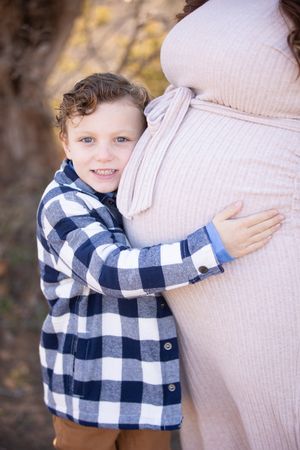 A child in a blue and white plaid shirt hugs a person wearing a beige sweater in an outdoor setting.