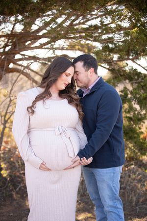 A couple shares an intimate moment outdoors during a maternity photo session in winter.