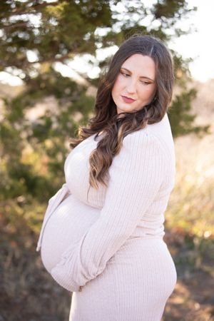 A person in a white knit sweater poses outdoors during golden hour with warm natural lighting.