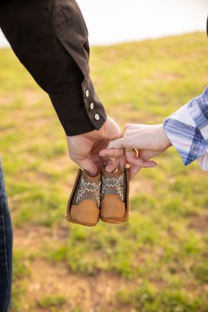 Close-up view of two people holding hands in a grassy outdoor setting.