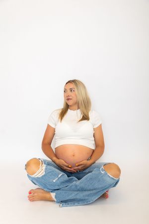 A person wearing a white crop top and blue jeans sits in various relaxed poses against a white background.