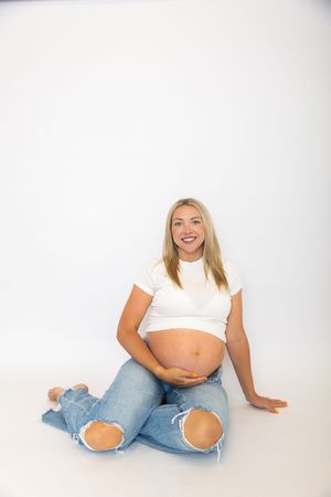 Sequence of pregnancy progression photos showing growing belly in white top and ripped jeans against white background.