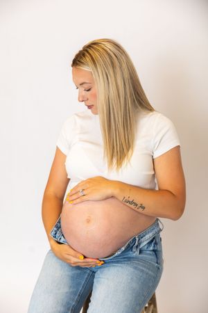 Expectant mother in white t-shirt and jeans lovingly cradles her pregnant belly against white background.