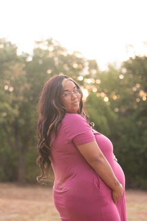 A person in a bright pink shirt poses outdoors during golden hour with trees in the background.