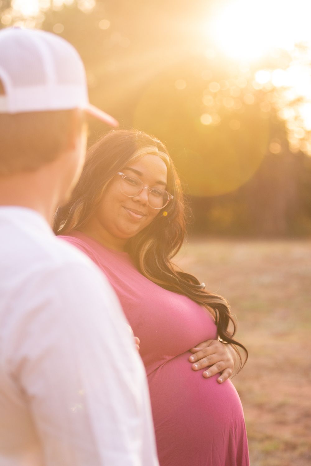 A couple shares an intimate moment at sunset while celebrating their pregnancy in a warm golden-hour setting.