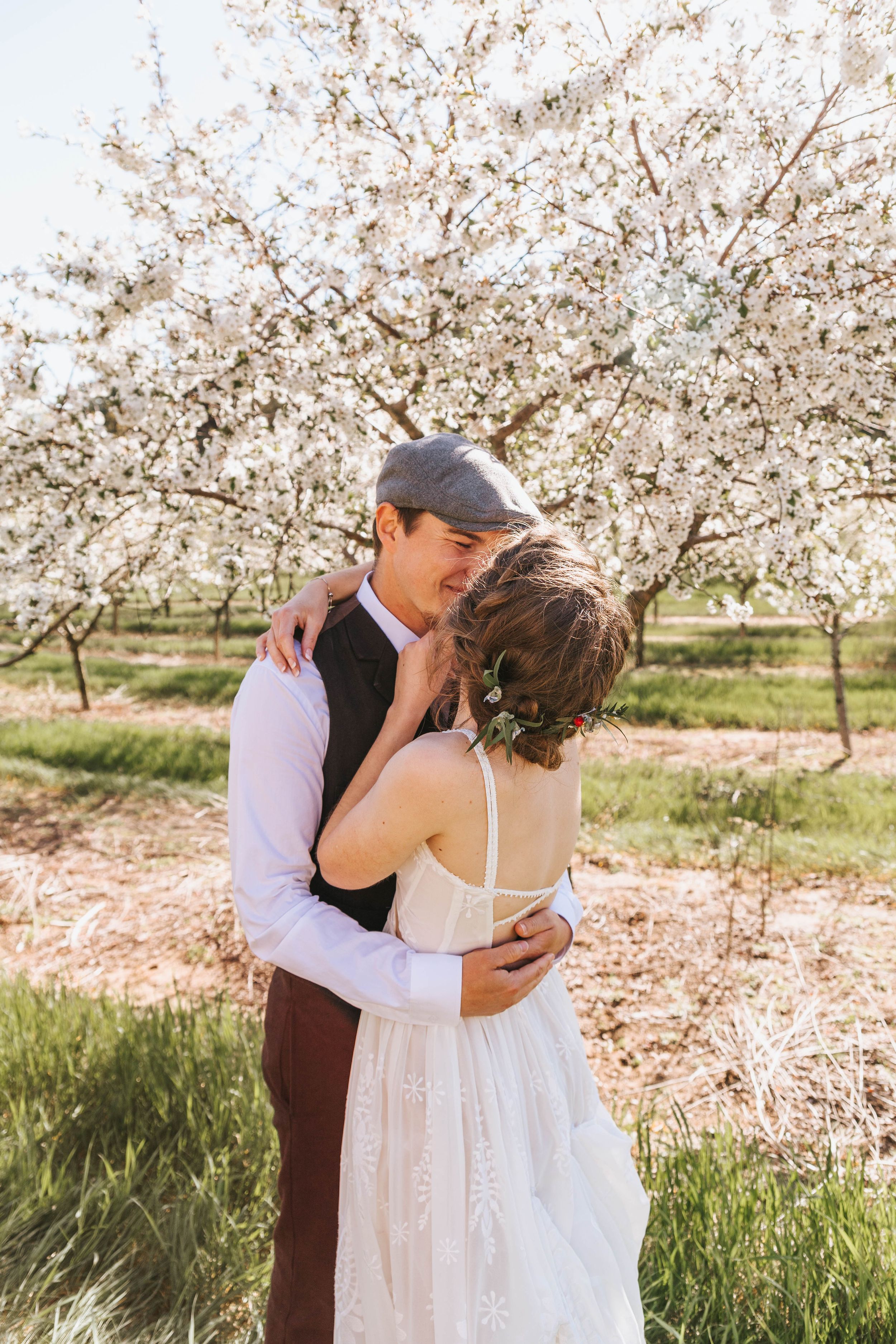 Intimate moment captured between couple surrounded by delicate spring blossoms in an orchard.