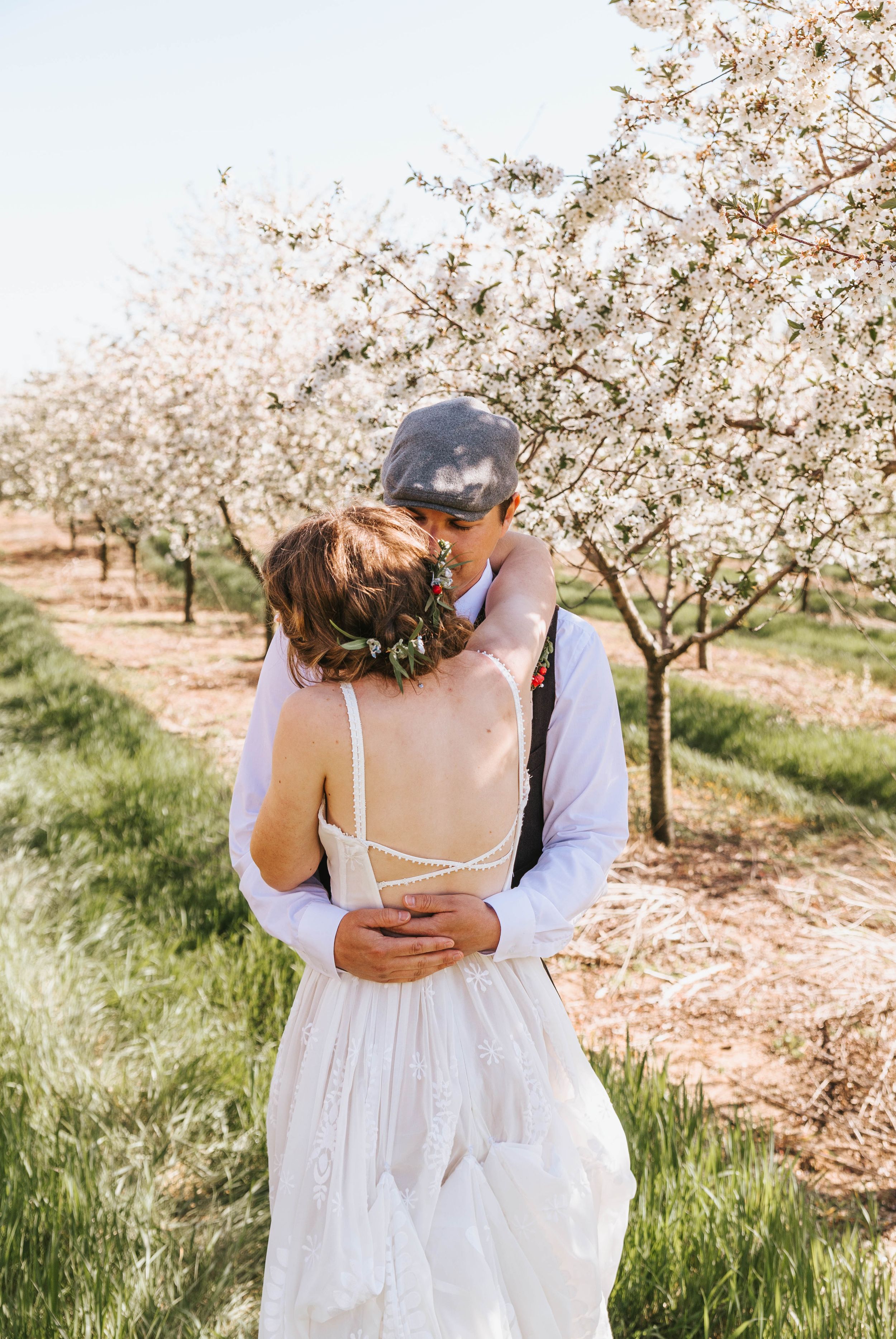 Couple embraces under blooming cherry blossom trees in a romantic spring orchard setting.
