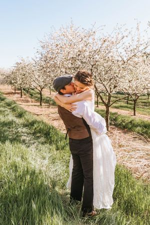 Romantic couple sharing tender moments among flowering trees in springtime orchard.