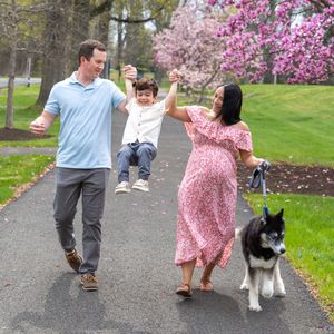 A couple and their husky dog take a joyful walk together under blooming cherry blossom trees in springtime.