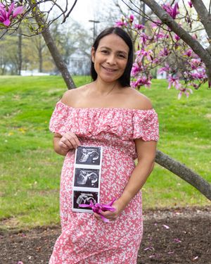 A springtime maternity photo showing ultrasound images while standing near blooming pink flowers.