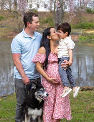 Family and their black and white dog pose together by a lake on a spring day.