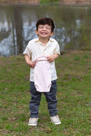 A candid outdoor photo by a pond showing a small pink baby onesie being held up with joy.