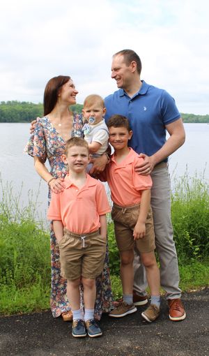 A family of five poses together by a lake, wearing coordinated outfits of coral, blue and floral prints.