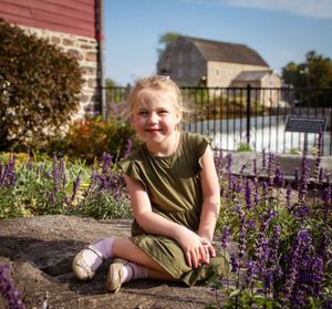 A person poses in front of a garden with purple salvia flowers on a sunny autumn day.