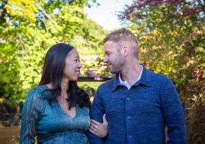 A couple shares a joyful moment together outdoors surrounded by vibrant autumn foliage and sunlight.