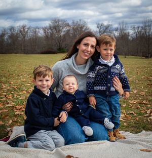 Family members lounging together on a blanket in autumn field with fallen leaves.