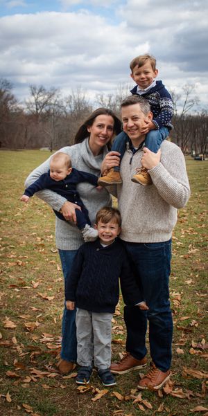Casual family portrait in coordinated sweaters on grassy field with autumn leaves.