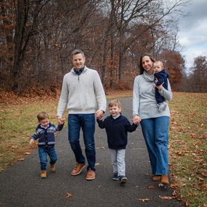 A family walks together on a paved path through autumn foliage on an overcast day.