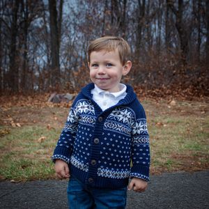 Child wearing navy blue and white patterned sweater standing outdoors in fall setting.