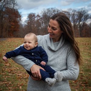 Parent and child playing together in fallen autumn leaves on a cloudy day.
