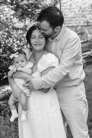 Black and white portrait of a couple embracing while holding their newborn baby outdoors.
