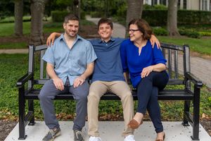 Three smiling people sitting together on a black metal bench outdoors in a park setting.