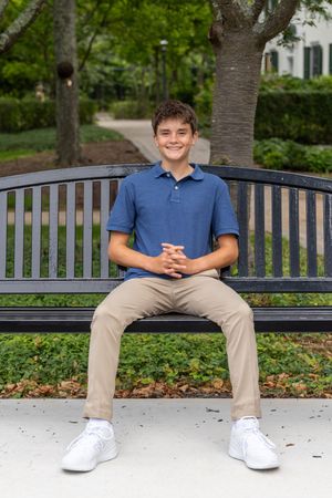 Smiling teenage boy in blue polo and khaki pants sitting on a park bench outdoors.